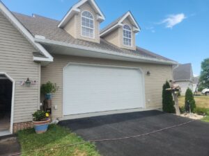 A house with a white garage door, beige siding, and decorative plants outside.